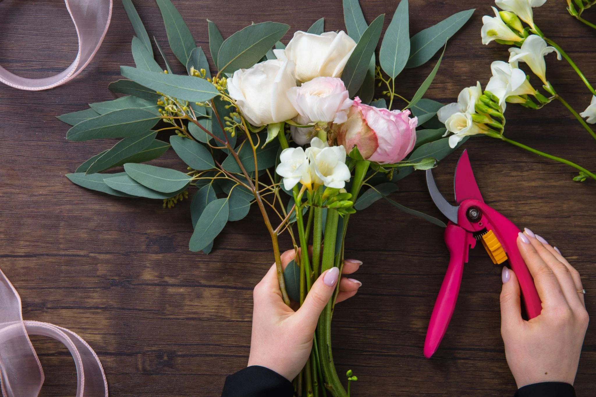 Florist holding fresh flower stems beside pruning shears on a wooden worktable